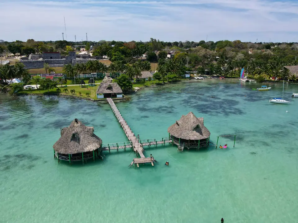 a group of huts on a dock over a body of water with Xelha in the background — Bacalar