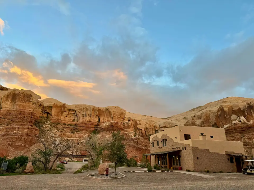 A tan adobe building beneath towering red sandstone cliffs under a soft blue and orange sky — Valle de Guadalupe
